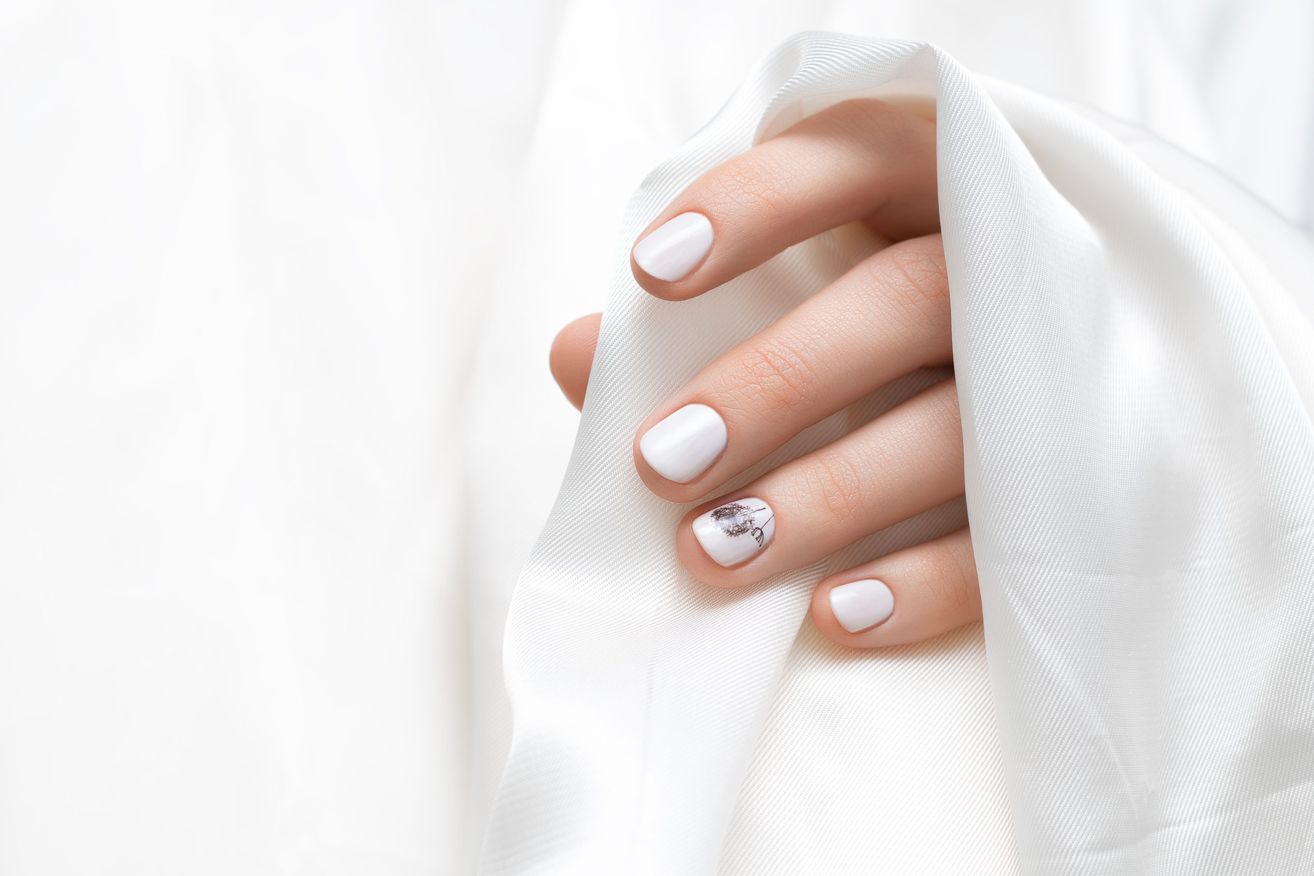 Female hand with white dandelion nail design